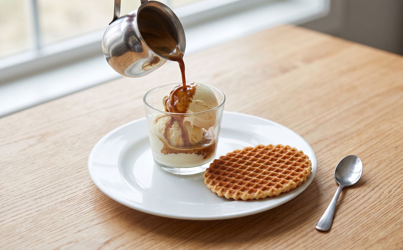 Espresso being poured over vanilla gelato in a glass, with a large waffle crisp on the plate