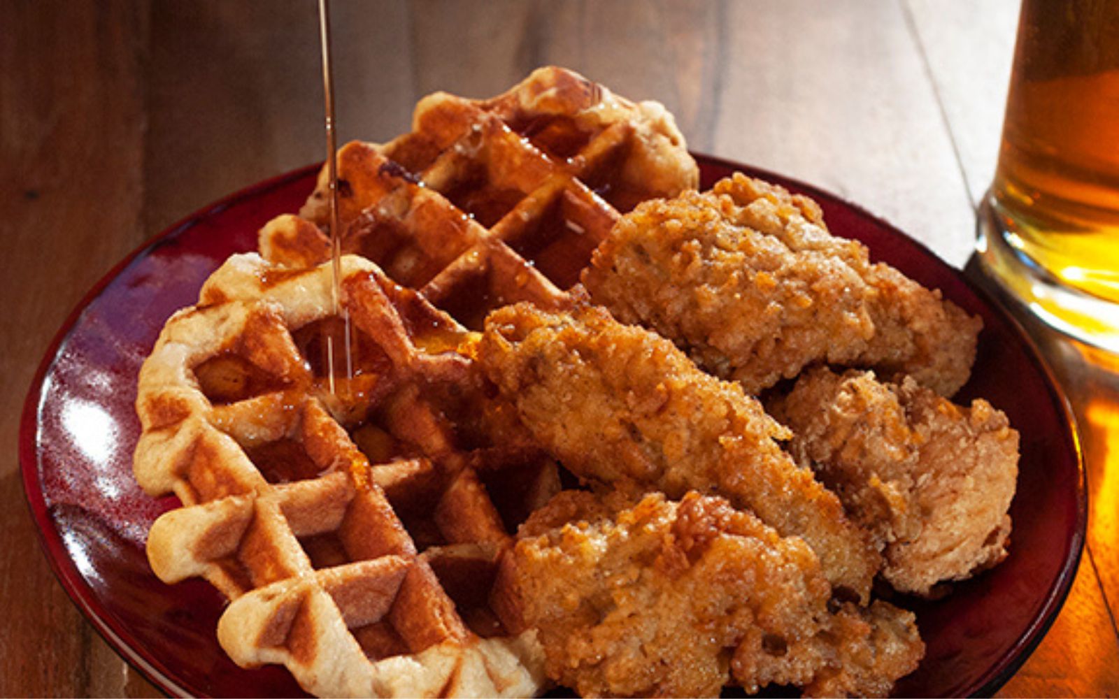 Crispy chicken tenders on Liège waffles with syrup being drizzled over the plate